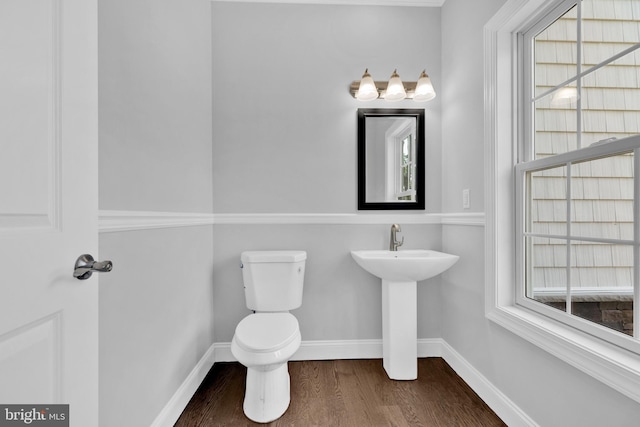 half bath with a wealth of natural light, toilet, baseboards, and wood finished floors