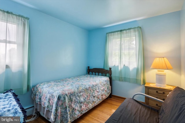 bedroom featuring multiple windows, baseboard heating, and light hardwood / wood-style flooring