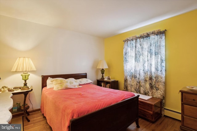 bedroom featuring a baseboard heating unit and wood-type flooring