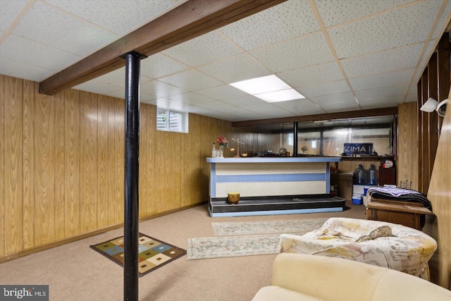 basement with light carpet, a paneled ceiling, and wood walls