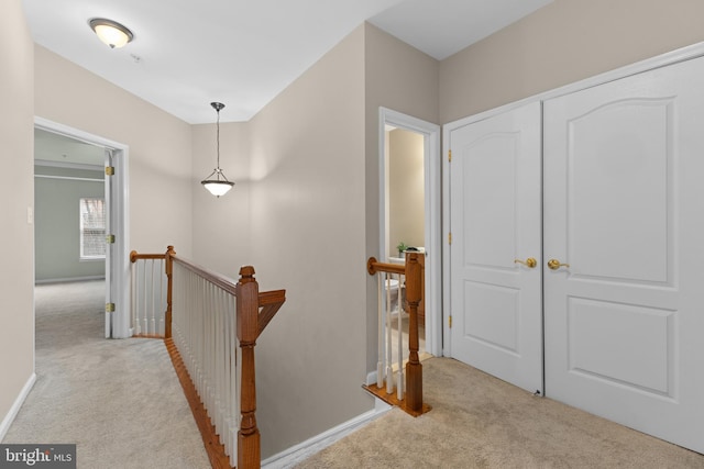 hallway featuring light carpet, an upstairs landing, and baseboards