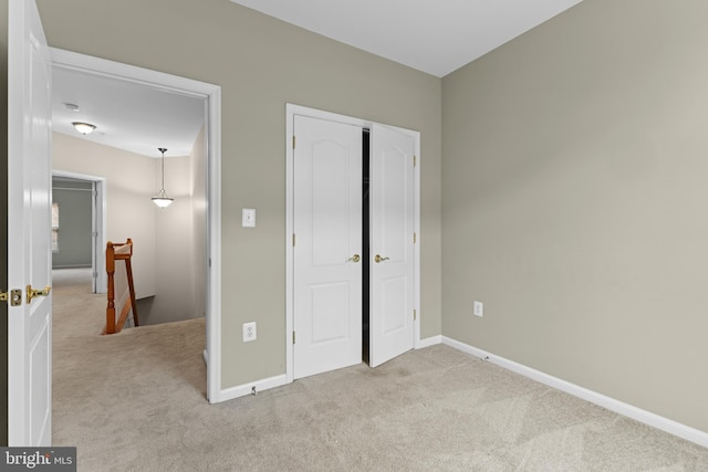 unfurnished bedroom featuring a closet, light carpet, and baseboards