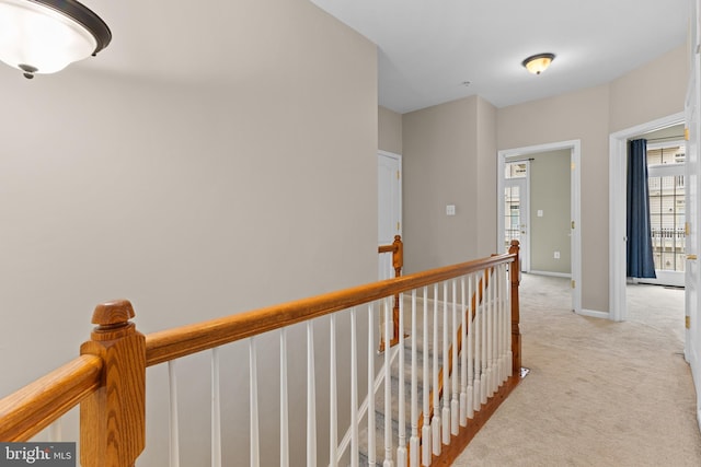 hallway featuring light carpet, an upstairs landing, and baseboards