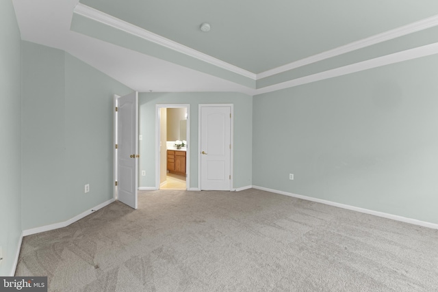 unfurnished bedroom with ensuite bathroom, light colored carpet, baseboards, ornamental molding, and a tray ceiling