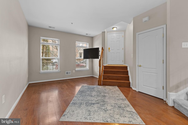 interior space featuring wood finished floors, visible vents, baseboards, and stairs