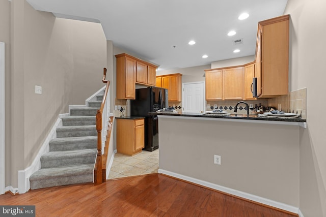 kitchen with tasteful backsplash, dark countertops, visible vents, a peninsula, and black fridge