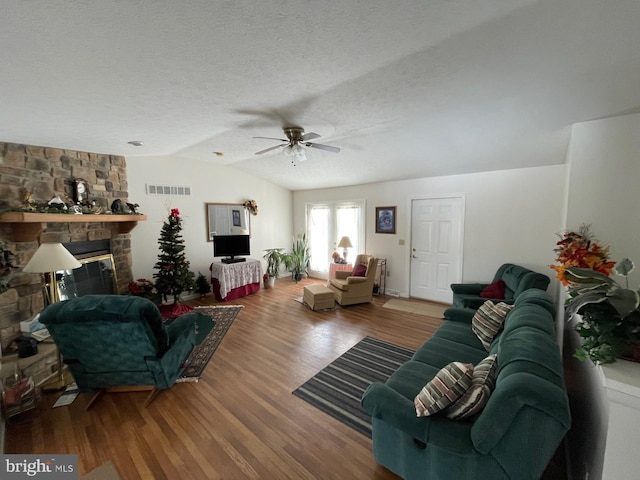 living room with lofted ceiling, hardwood / wood-style flooring, ceiling fan, a textured ceiling, and a stone fireplace