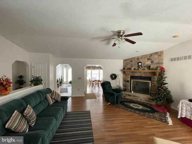 living room featuring hardwood / wood-style floors, a fireplace, lofted ceiling, ceiling fan, and a textured ceiling