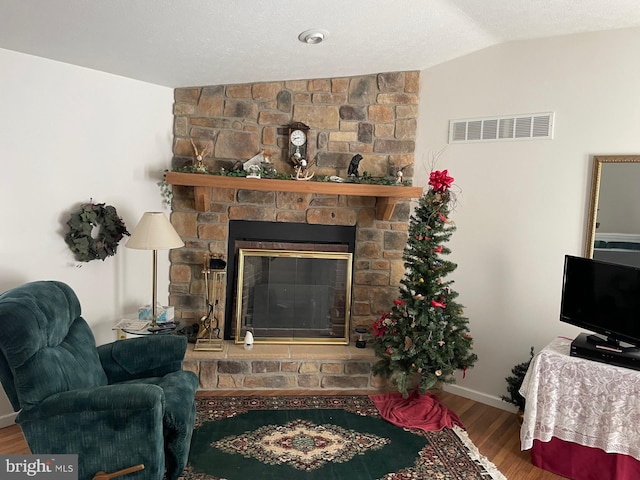 living room with lofted ceiling, a stone fireplace, hardwood / wood-style floors, and a textured ceiling