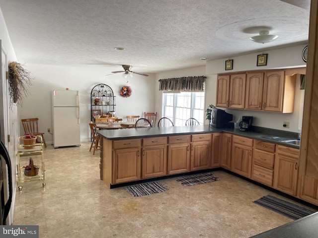 kitchen featuring ceiling fan, kitchen peninsula, white fridge, and a textured ceiling