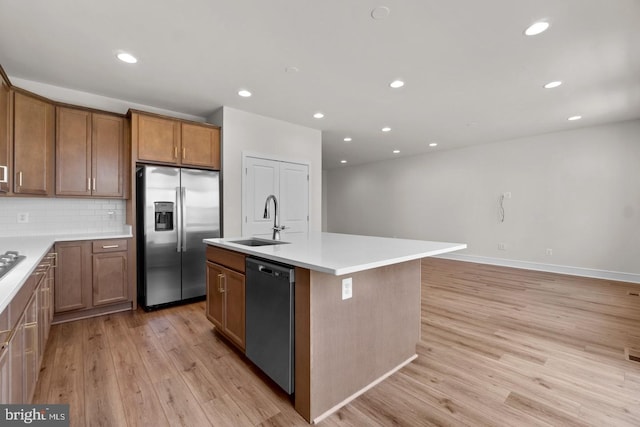 kitchen featuring a center island with sink, appliances with stainless steel finishes, brown cabinets, light countertops, and a sink