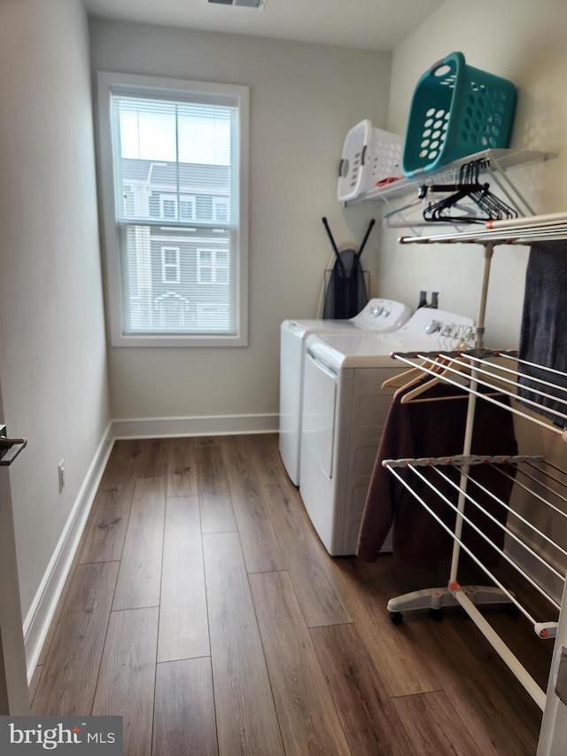 clothes washing area with laundry area, wood finished floors, washing machine and dryer, and baseboards