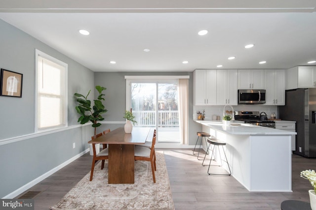 kitchen with stainless steel appliances, tasteful backsplash, light hardwood / wood-style floors, an island with sink, and white cabinets