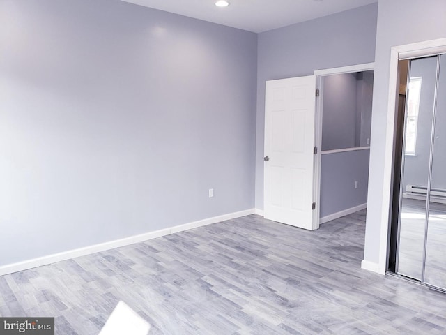 unfurnished room with a baseboard heating unit and light wood-type flooring