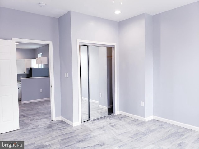 unfurnished bedroom featuring light hardwood / wood-style floors, a closet, and refrigerator