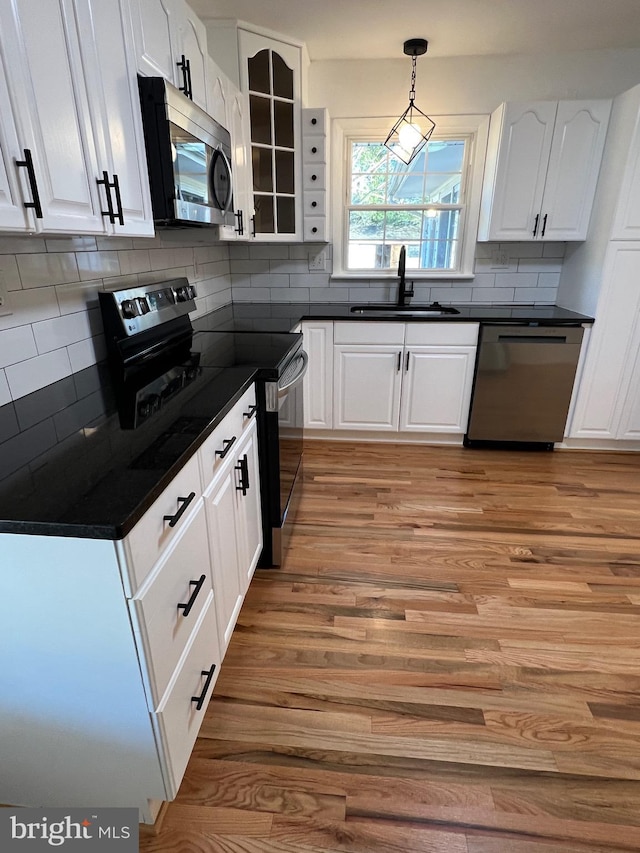 kitchen with stainless steel appliances, dark countertops, glass insert cabinets, white cabinets, and a sink