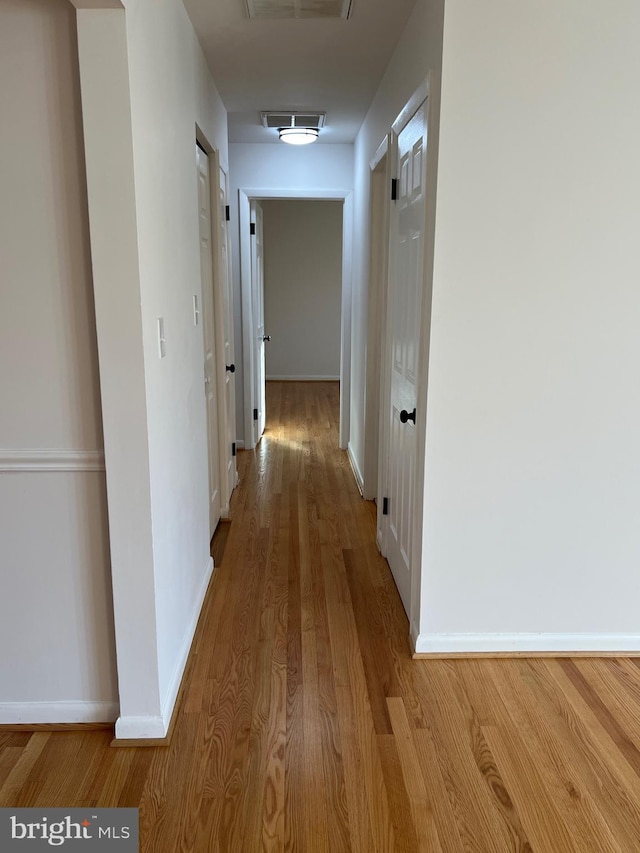 hallway with light wood finished floors, visible vents, and baseboards