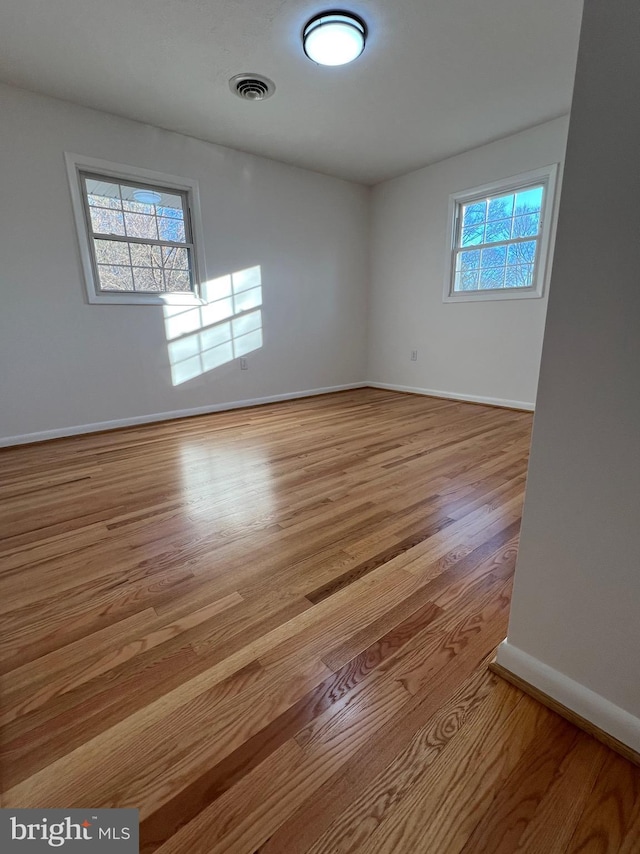 empty room with light wood-type flooring, plenty of natural light, visible vents, and baseboards