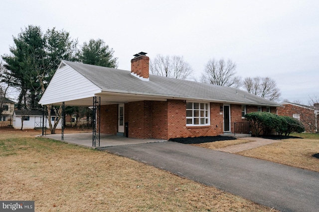 ranch-style home with brick siding, a chimney, aphalt driveway, an attached carport, and a front yard