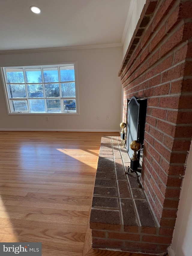 unfurnished living room with brick wall, a fireplace, wood finished floors, baseboards, and crown molding