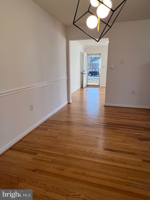 unfurnished dining area with a notable chandelier, wood finished floors, and baseboards