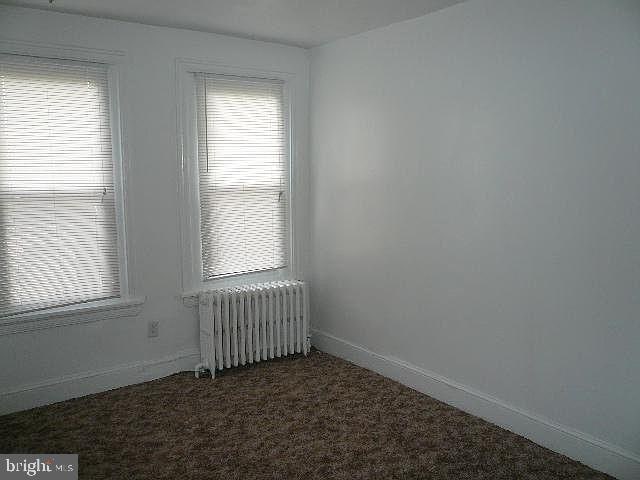 unfurnished room featuring radiator heating unit and dark colored carpet