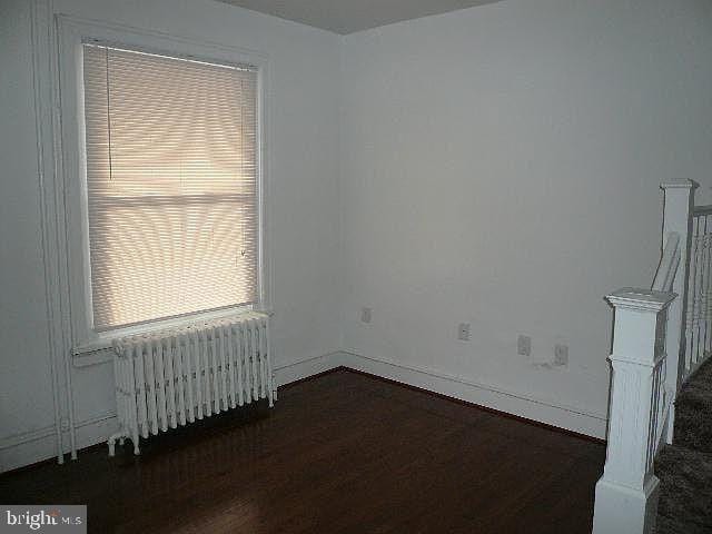 empty room with dark hardwood / wood-style floors and radiator heating unit