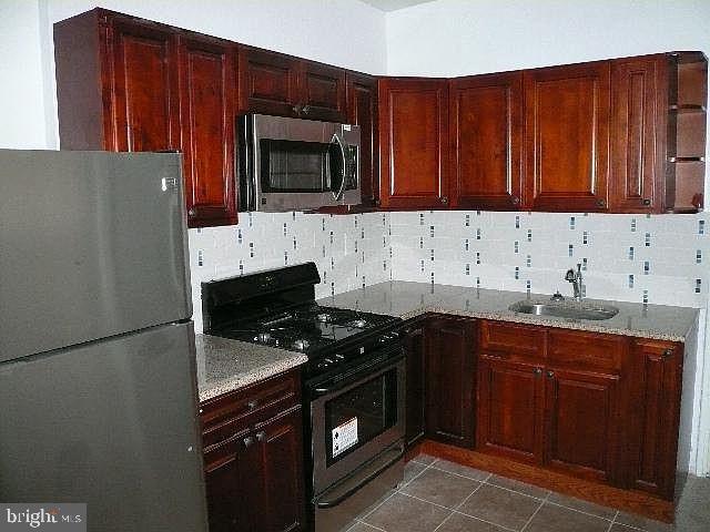 kitchen featuring stainless steel appliances, sink, backsplash, and light stone counters