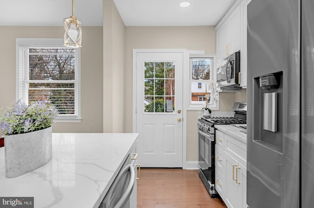 kitchen featuring light stone counters, decorative light fixtures, light wood-type flooring, stainless steel appliances, and white cabinets