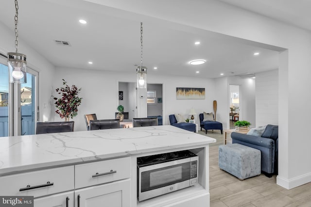 kitchen featuring pendant lighting, light stone counters, plenty of natural light, and white cabinets