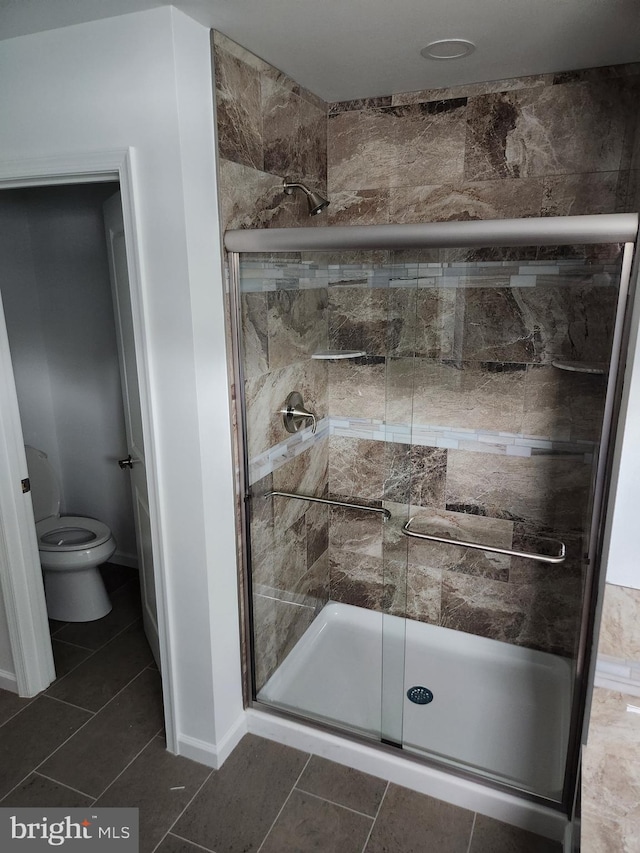 bathroom featuring tile patterned floors, a shower with door, and toilet