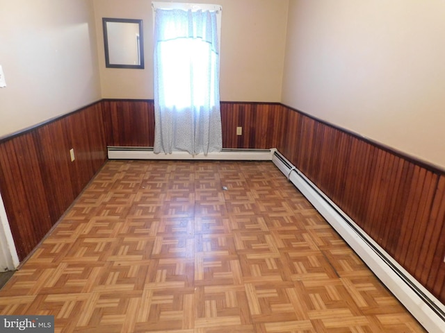 unfurnished room with wooden walls, baseboard heating, and wainscoting