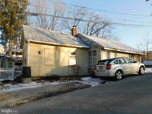 snow covered property featuring metal roof and a chimney