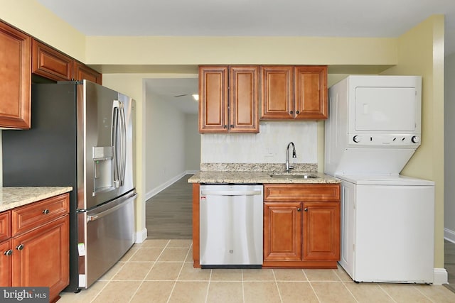 kitchen with stacked washing maching and dryer, appliances with stainless steel finishes, sink, light tile patterned floors, and light stone countertops