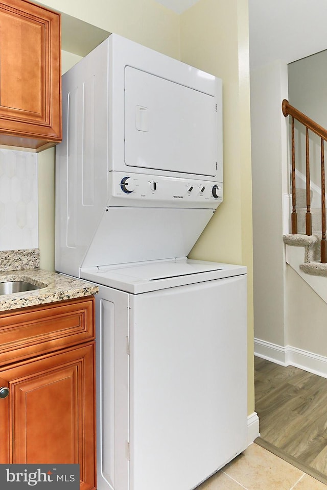 laundry room featuring cabinets, stacked washer and dryer, and light tile patterned floors