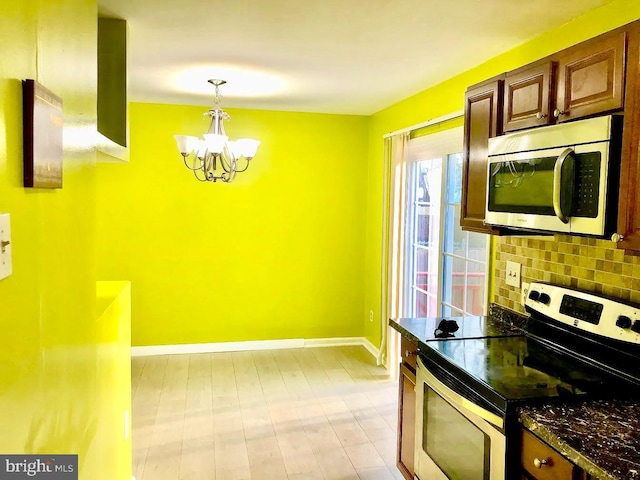 kitchen featuring dark stone countertops, hanging light fixtures, stainless steel appliances, a notable chandelier, and decorative backsplash