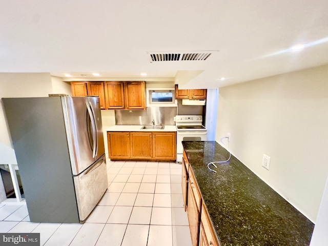 kitchen featuring white electric range, stainless steel refrigerator, sink, dark stone countertops, and light tile patterned floors