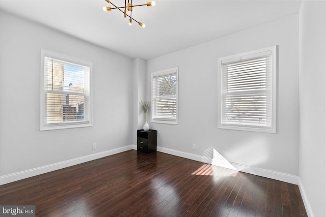 empty room with dark wood-type flooring and a notable chandelier