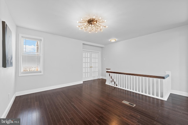 spare room with dark hardwood / wood-style floors, a chandelier, and french doors