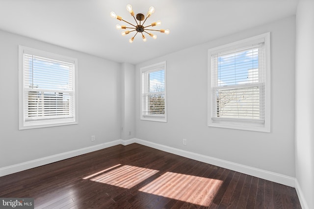 spare room featuring dark wood-type flooring and a notable chandelier