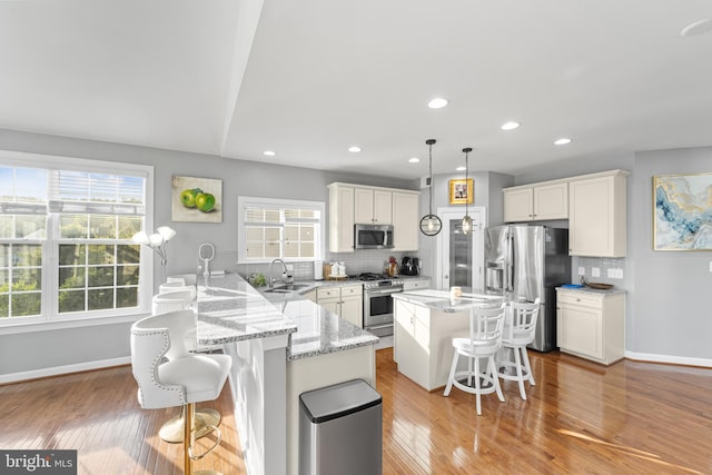 kitchen featuring decorative light fixtures, stainless steel appliances, a center island, and a breakfast bar