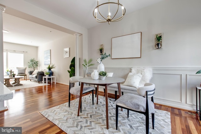 dining space featuring an inviting chandelier, decorative columns, and light wood-type flooring