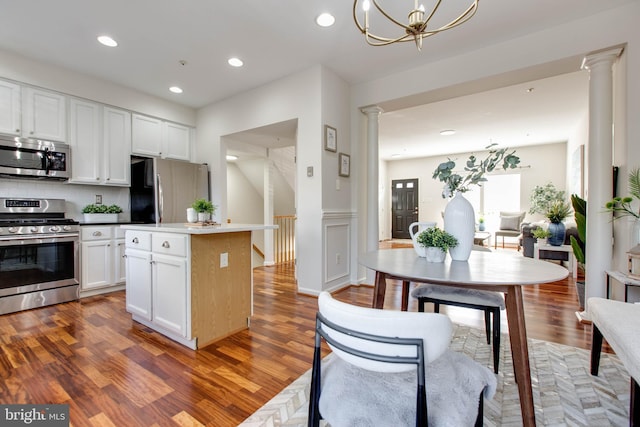 kitchen featuring dark wood-type flooring, stainless steel appliances, decorative columns, white cabinets, and a kitchen island