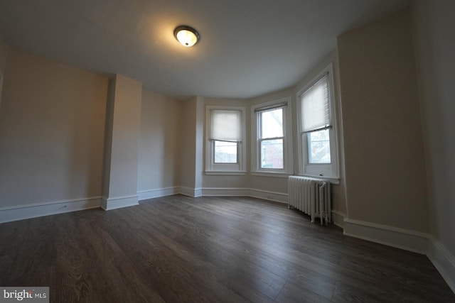 empty room with radiator heating unit and dark hardwood / wood-style flooring