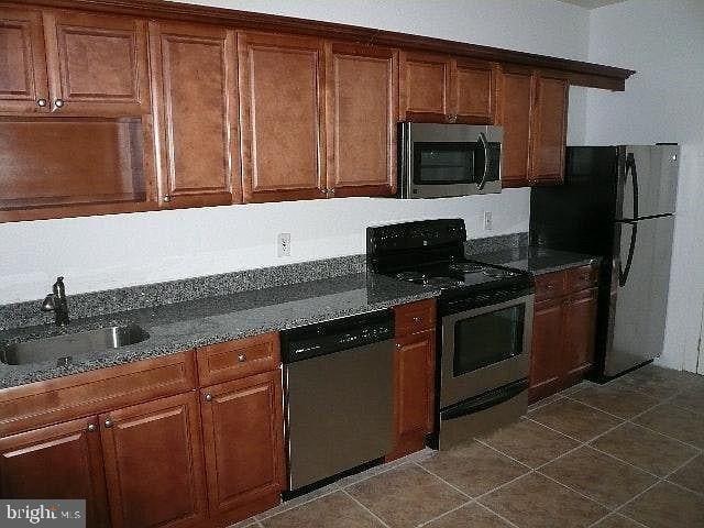 kitchen with dark stone countertops, sink, dark tile patterned flooring, and appliances with stainless steel finishes