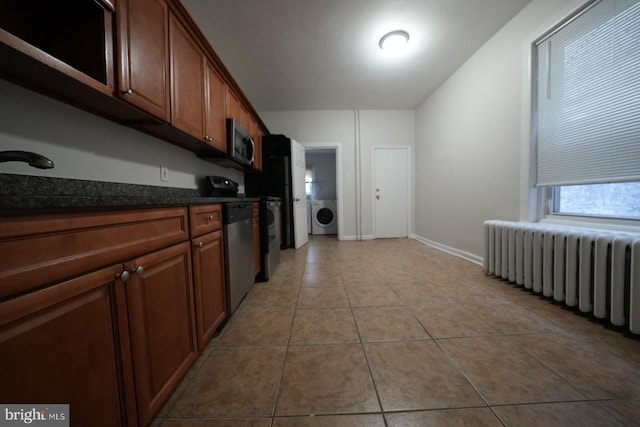 kitchen featuring light tile patterned floors, appliances with stainless steel finishes, dark stone countertops, radiator heating unit, and washer / clothes dryer