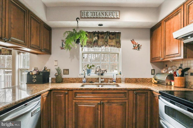 kitchen featuring sink, range hood, stainless steel appliances, light stone countertops, and decorative backsplash