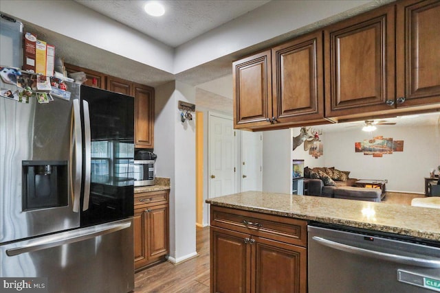 kitchen featuring light stone counters, stainless steel appliances, a textured ceiling, and light wood-type flooring