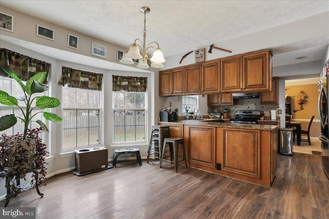 kitchen featuring stainless steel range with electric cooktop, decorative light fixtures, dark hardwood / wood-style flooring, kitchen peninsula, and exhaust hood