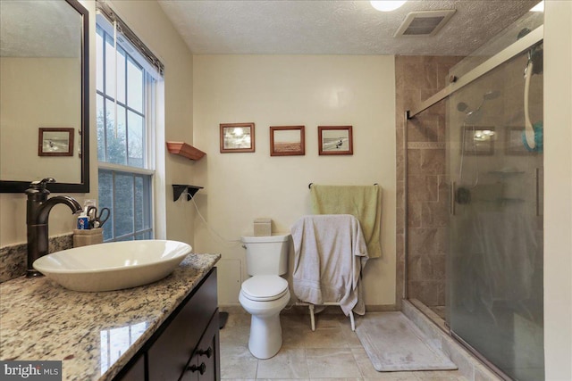 bathroom with a shower with door, vanity, a textured ceiling, and toilet